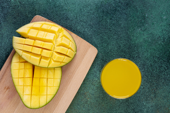 top view sliced mango on a blackboard with a glass of orange juice on a green background